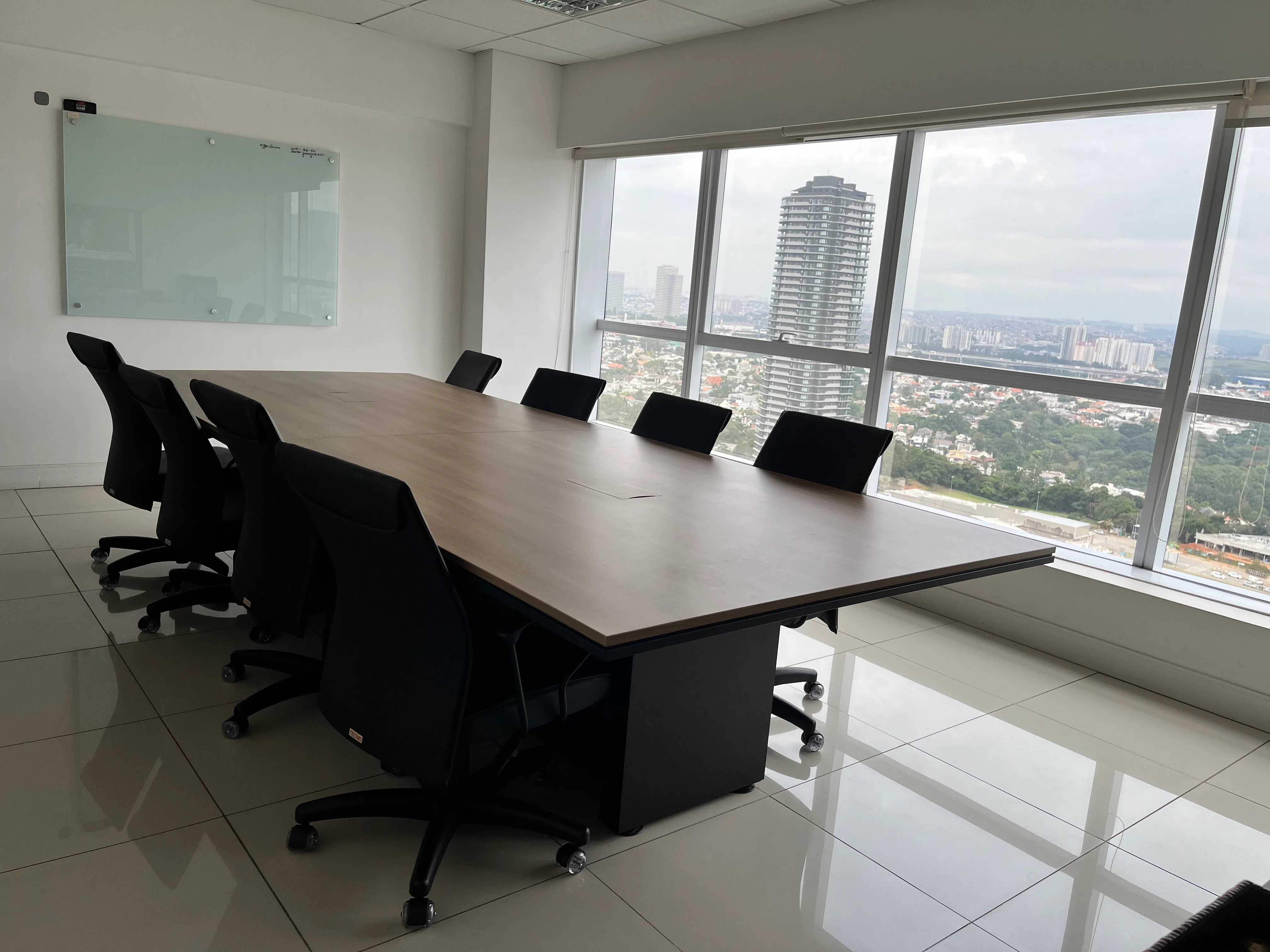 Vista geral da Sala K2 com mesa de reunião para 8 pessoas e janelas amplas